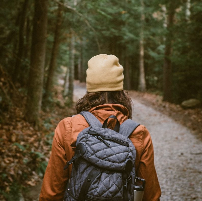 woman carrying backpack walking towards the forest